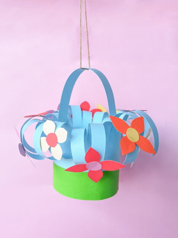 Hanging paper basket with blue curled strips, a green base, and colorful paper flowers
